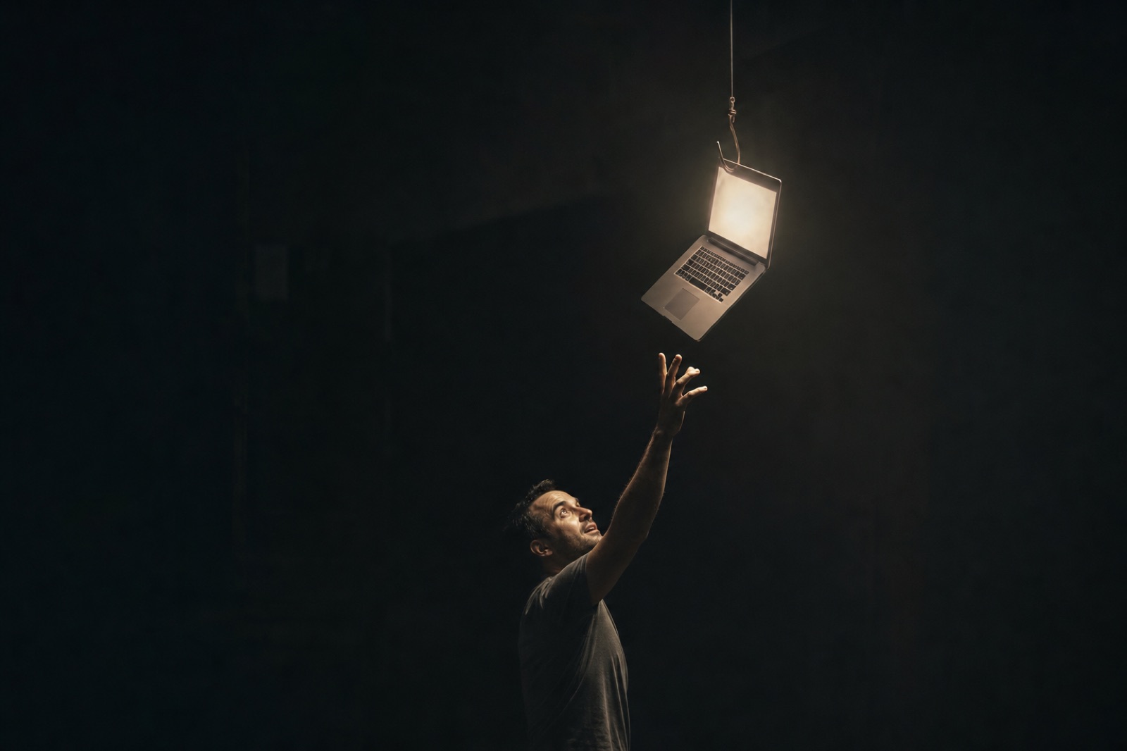 A man reaching up for a glowing laptop dangling like bait on a fishing line